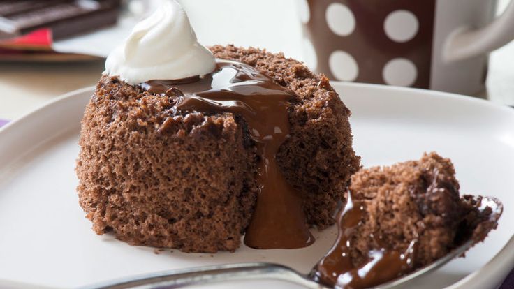 a piece of chocolate cake on a white plate with a fork next to it and a cup of coffee in the background