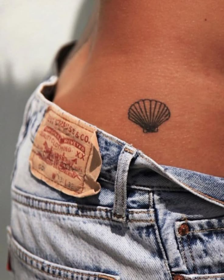 a woman's stomach with a small tattoo on her lower back, and a shell in the pocket