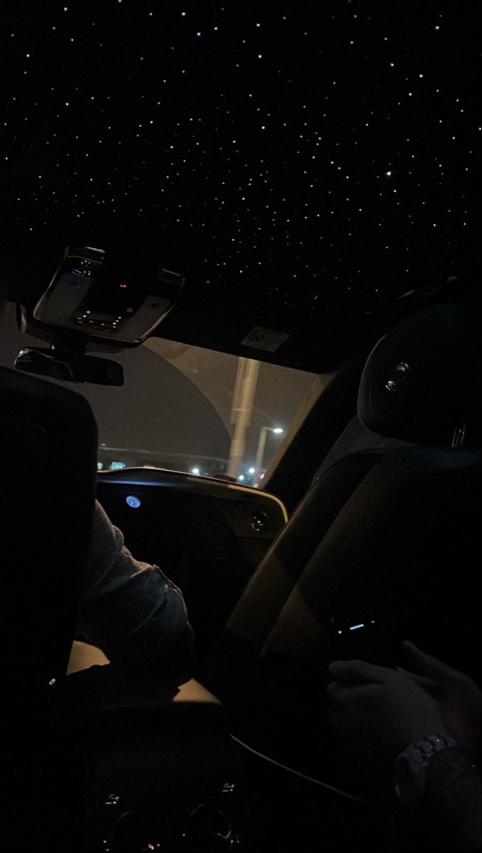 two people in a car at night with the stars on the ceiling and one person sitting behind the steering wheel