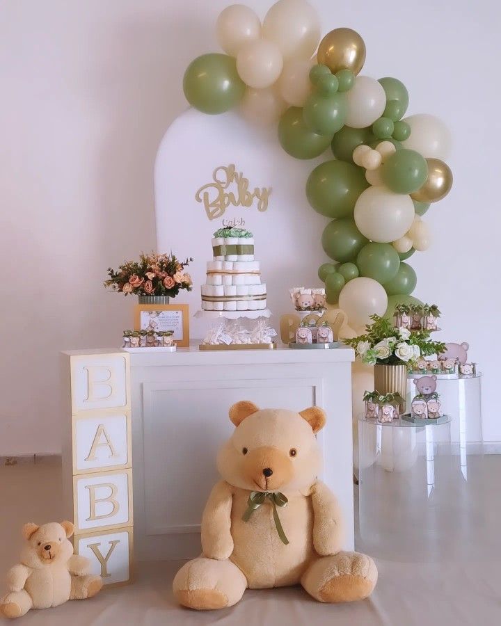 a teddy bear sitting in front of a table with balloons and cake on it's side