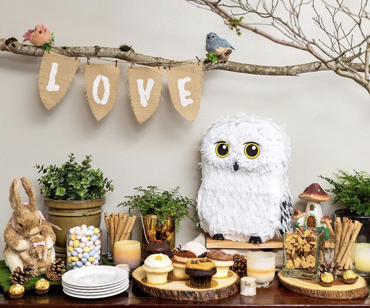 a table topped with an owl statue and other decorations on it's side next to a tree branch