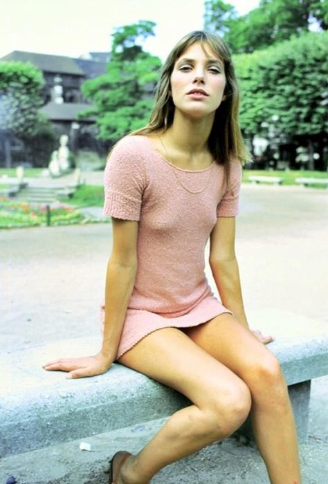 a woman sitting on a cement bench in a pink shirt and shorts with her legs crossed