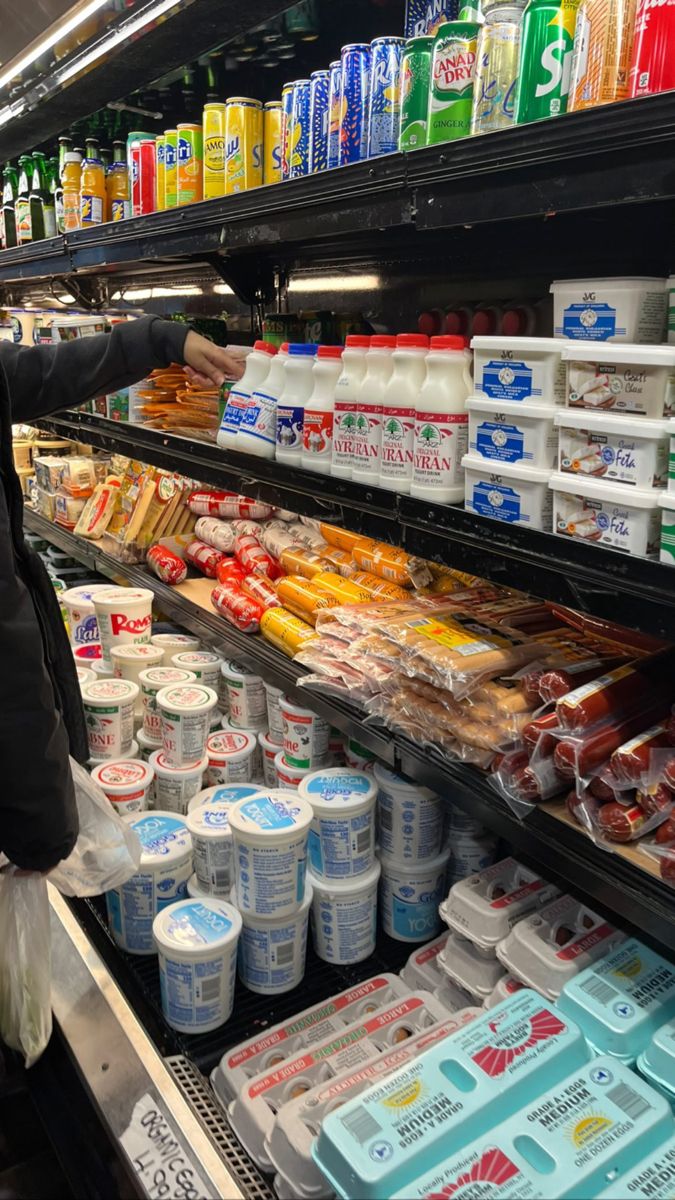 a woman is picking up some food from the shelf in a grocery store while she shops for groceries