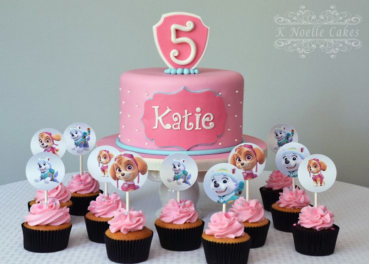 a pink birthday cake surrounded by cupcakes on a white tablecloth with the number five