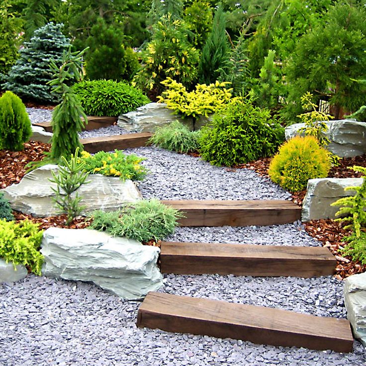 an outdoor garden with rocks, plants and stones on the ground in front of trees