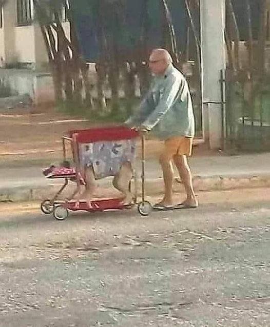 an older man pushing a baby carriage down the street with his foot on it's side