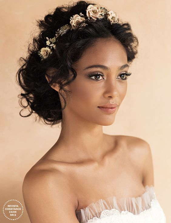 a woman with flowers in her hair wearing a white dress and looking at the camera