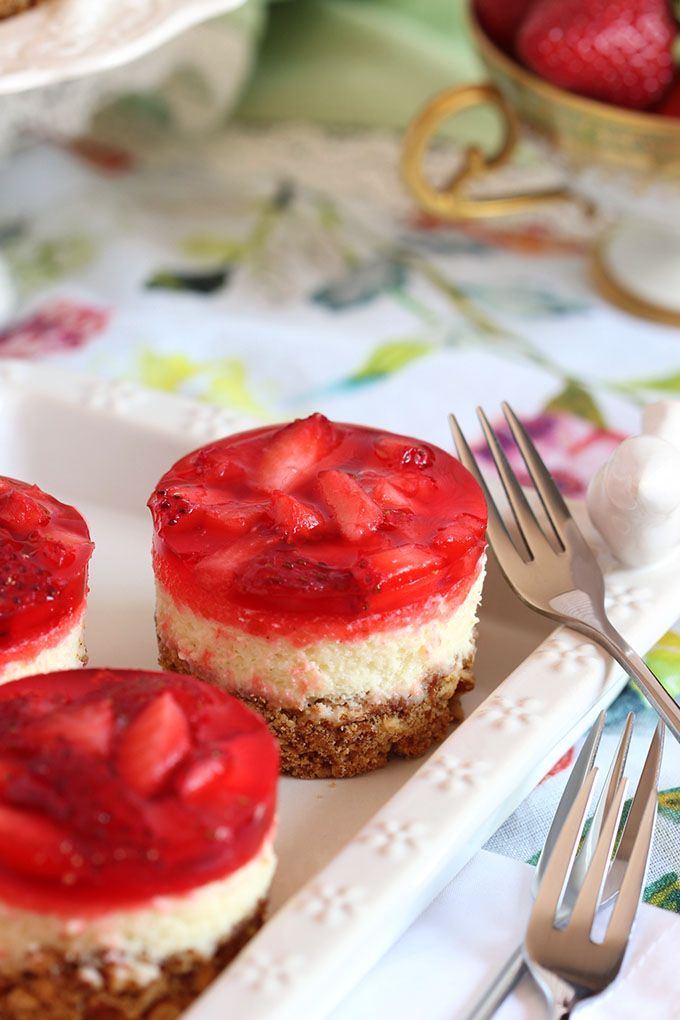 three desserts with strawberries are on a plate next to a fork and knife