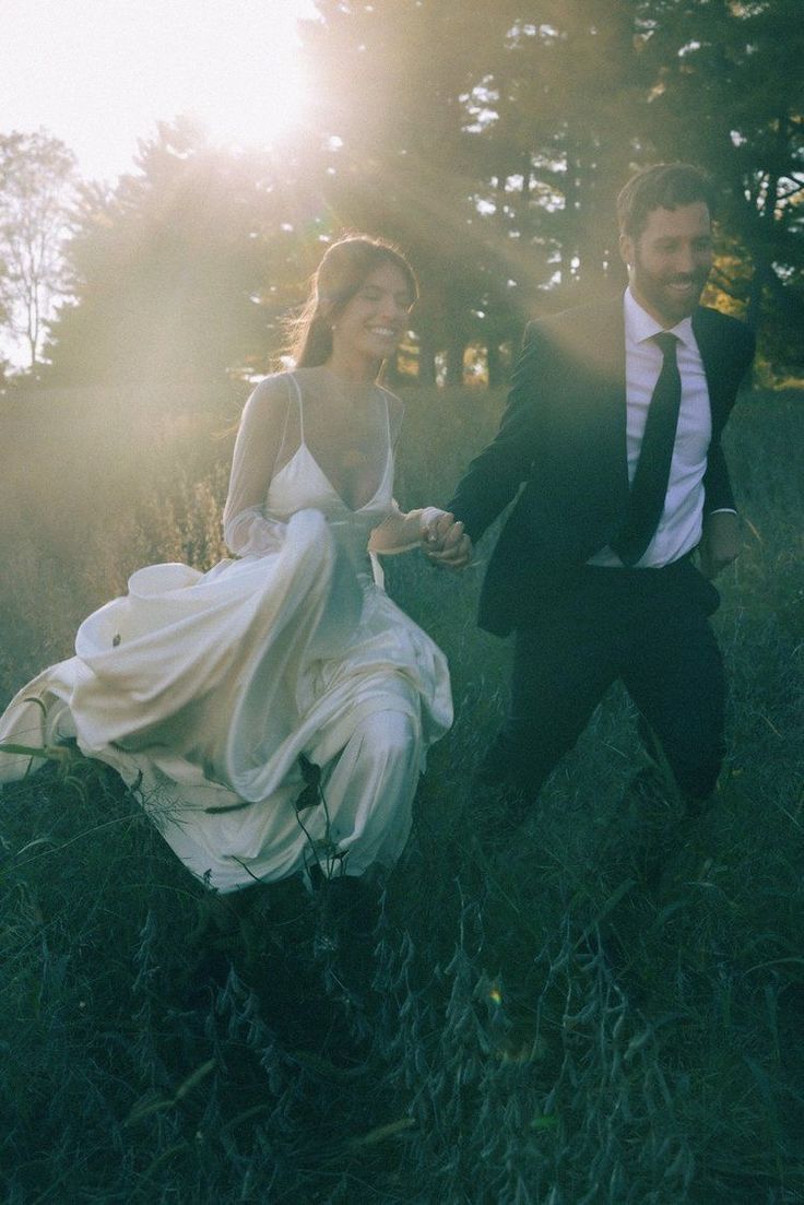 a man and woman in formal wear running through the grass with trees in the background