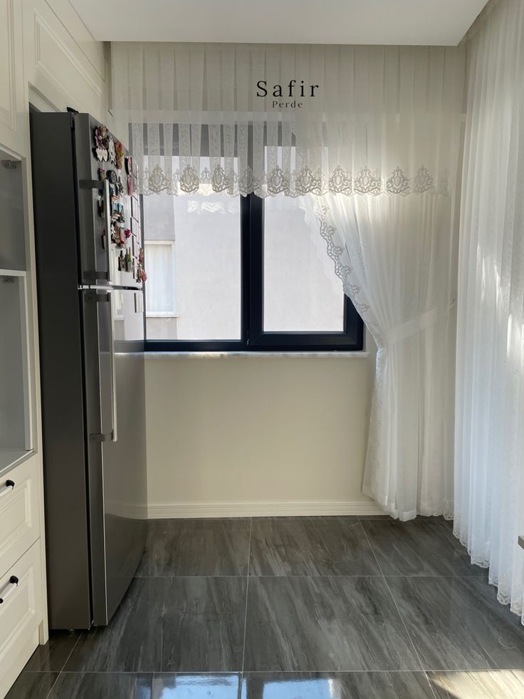 an empty kitchen with white curtains and gray tile flooring is seen in this image