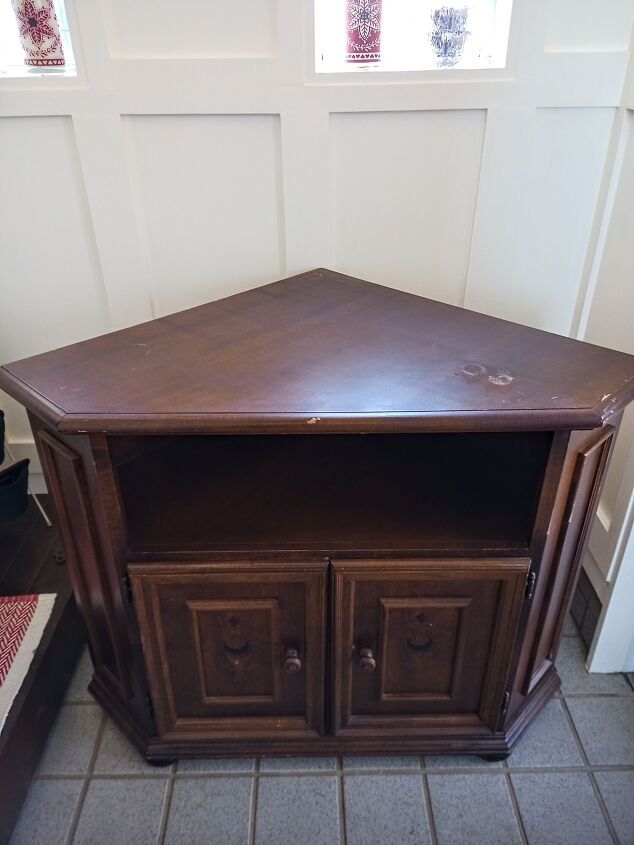 a wooden cabinet sitting on top of a tile floor next to a wall with two windows