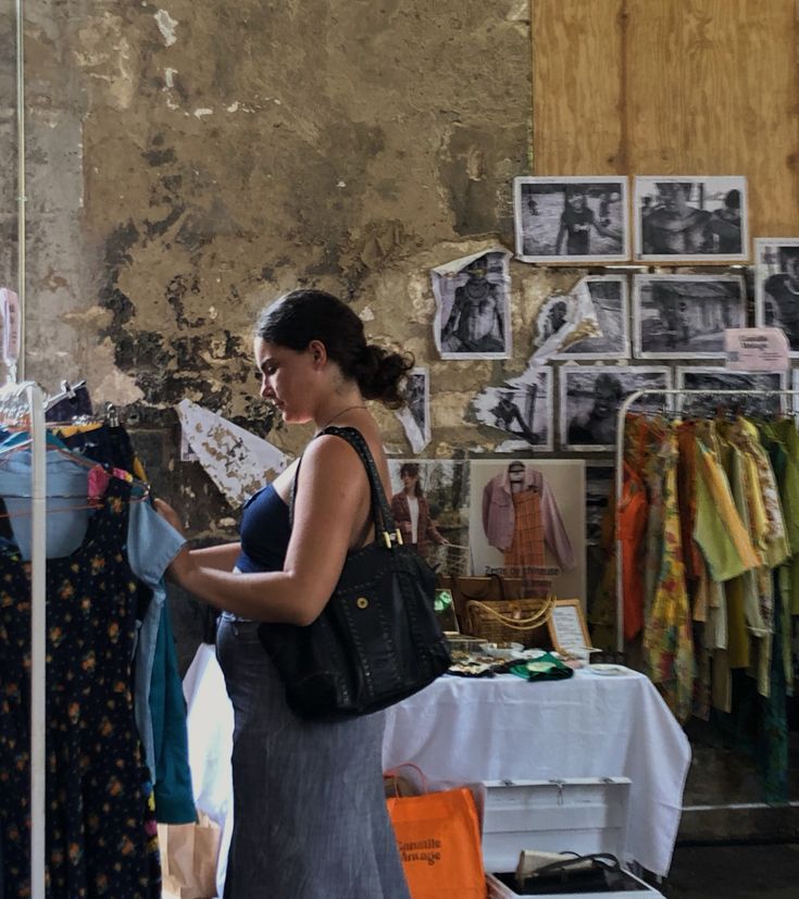 a woman standing in front of a table with clothes on it and pictures hanging up behind her