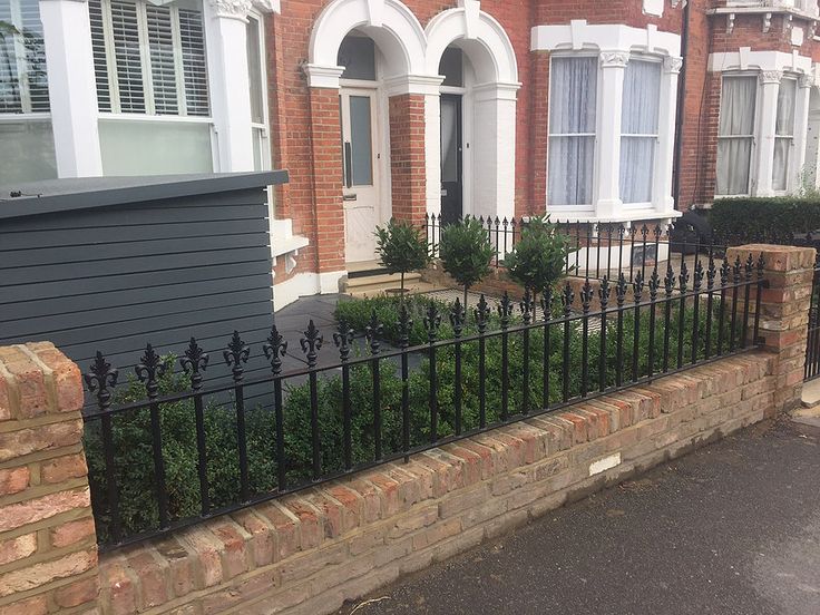 a black iron fence in front of a brick house with white windows and bushes behind it