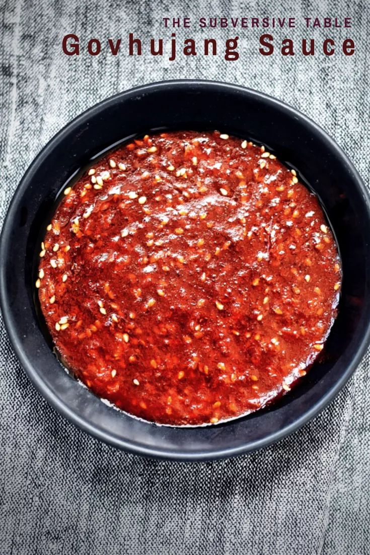 a black bowl filled with red sauce on top of a gray cloth covered tablecloth