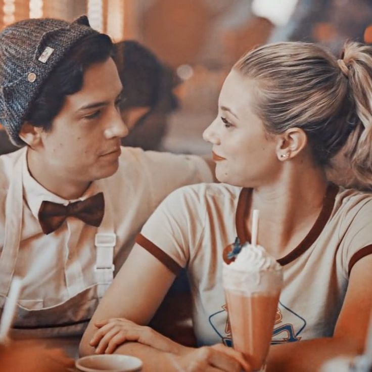 a man and woman sitting at a table with drinks in front of them, looking into each other's eyes