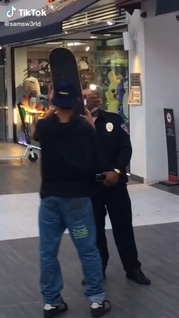 two men are standing in front of a store talking on their cell phones and one is holding a skateboard