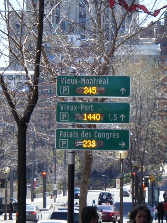 several street signs on the side of a busy city street with buildings in the background