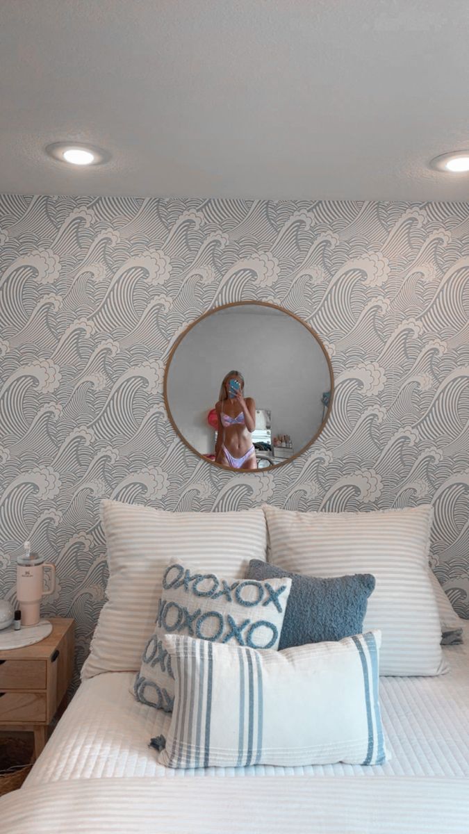 a woman sitting in front of a mirror on top of a bed with white sheets and pillows