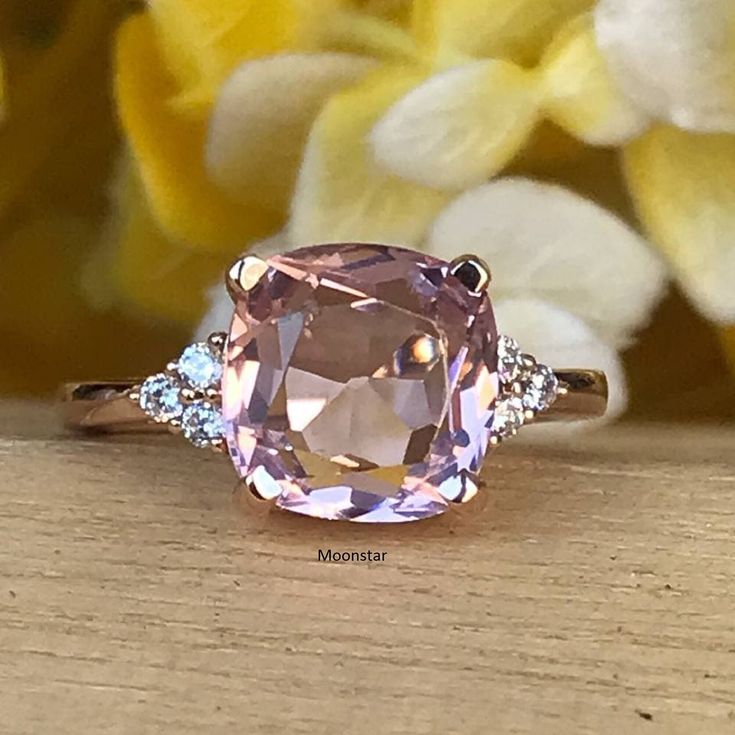 an oval cut pink sapphire and diamond ring on a wooden surface with flowers in the background