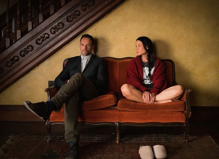 a man and woman sitting on top of a couch next to each other in front of a stair case