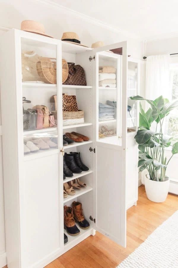 a white closet filled with lots of shoes and baskets on top of shelves next to a potted plant