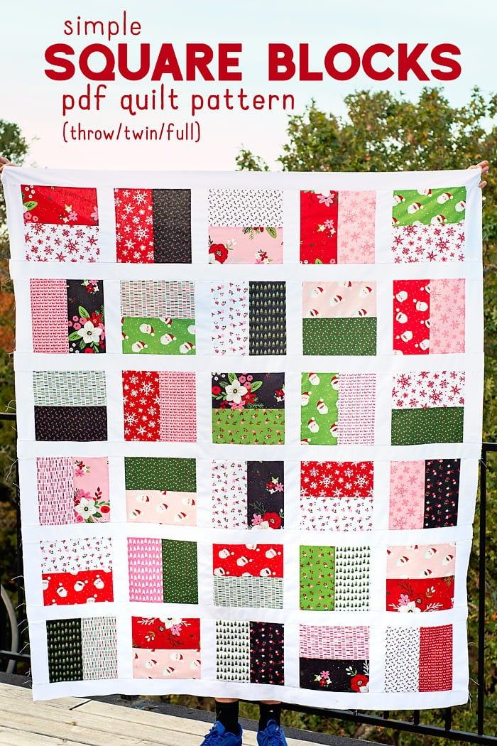 a quilt made with squares and flowers on top of a wooden bench in front of trees