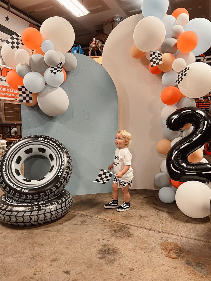 a little boy standing in front of some balloons and tire tires at a car show