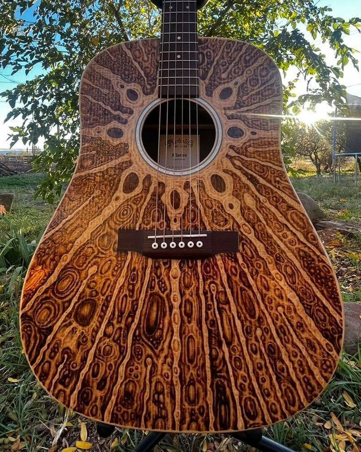 an acoustic guitar sitting in the grass under a tree