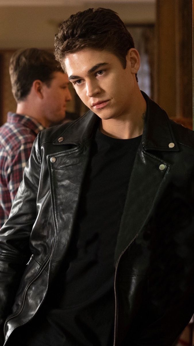 a young man in a black leather jacket sitting on a chair looking at the camera