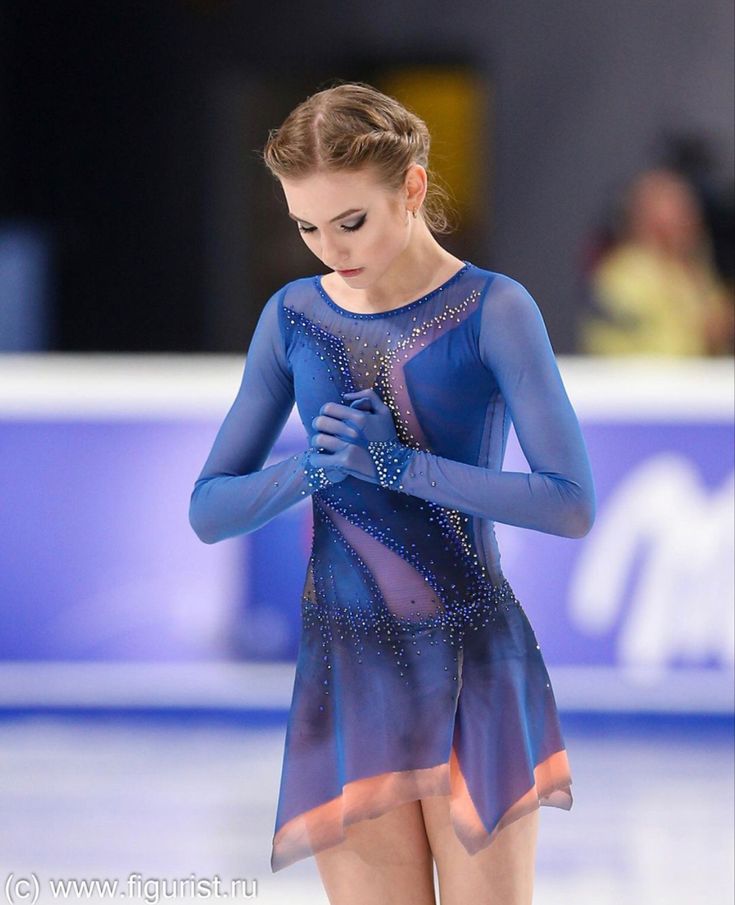 a female figure skating in a blue dress and holding her hand up to her chest