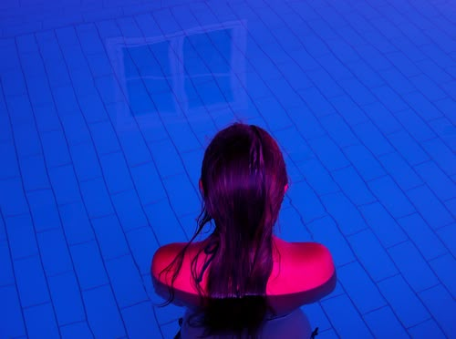 a woman sitting in the middle of a swimming pool with her back to the camera