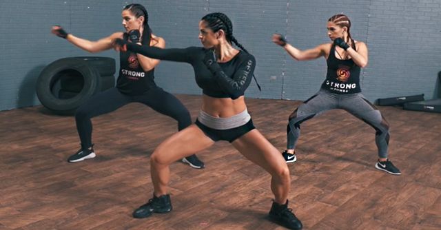 three women in black shirts and gray shorts are doing exercises on a wooden floor with one woman holding her arms out