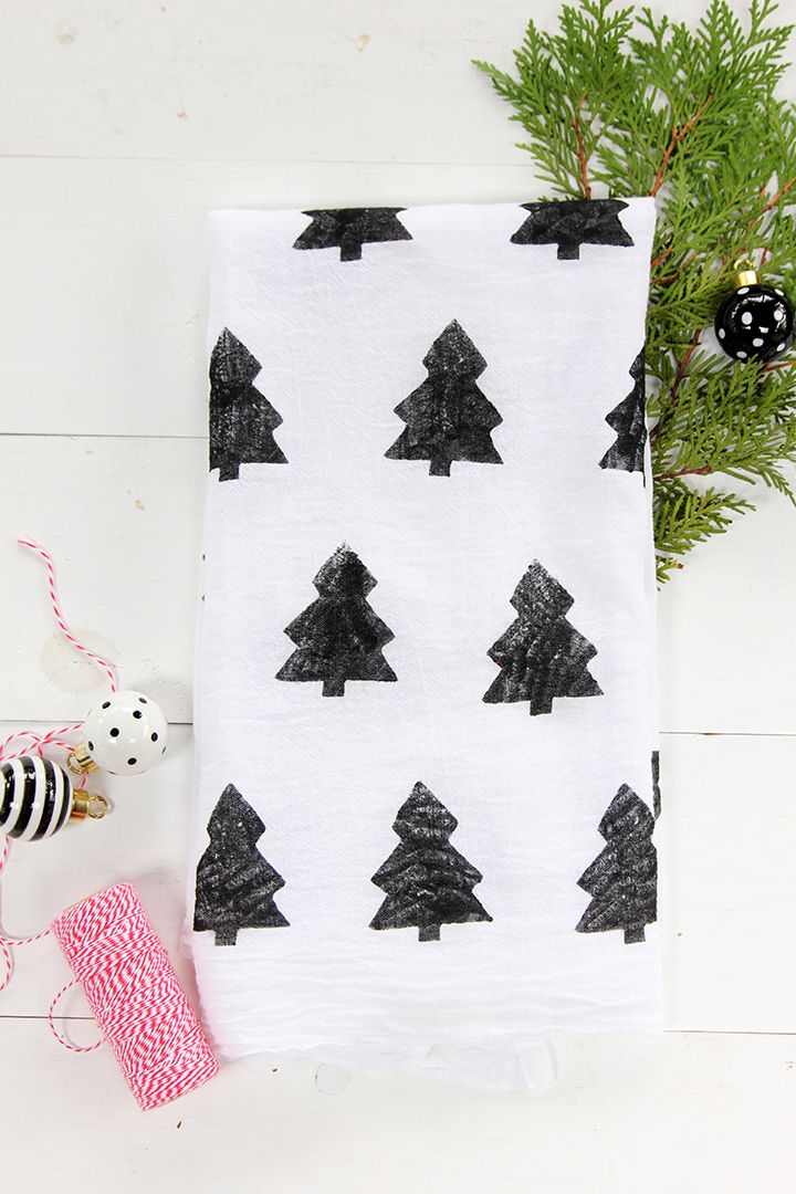 a black and white christmas tree tea towel on top of a wooden table next to a sprig of pine