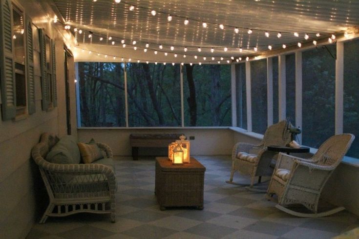 a screened porch with wicker furniture and string lights