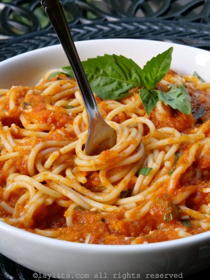 a white bowl filled with pasta and sauce on top of a black table next to a green leafy garnish