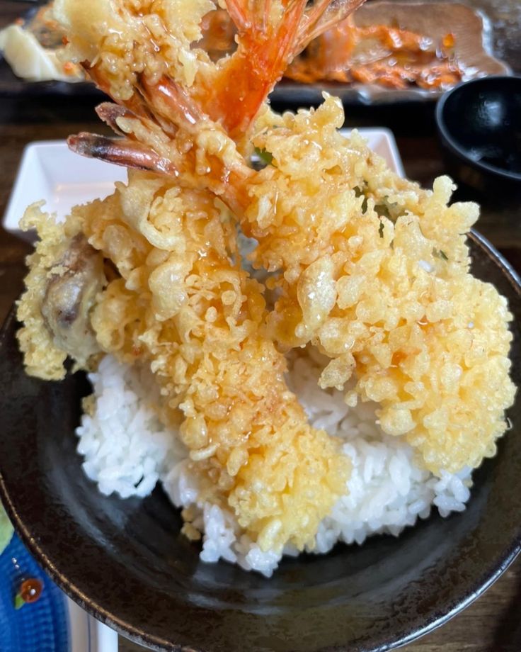 a black plate topped with rice covered in shrimp