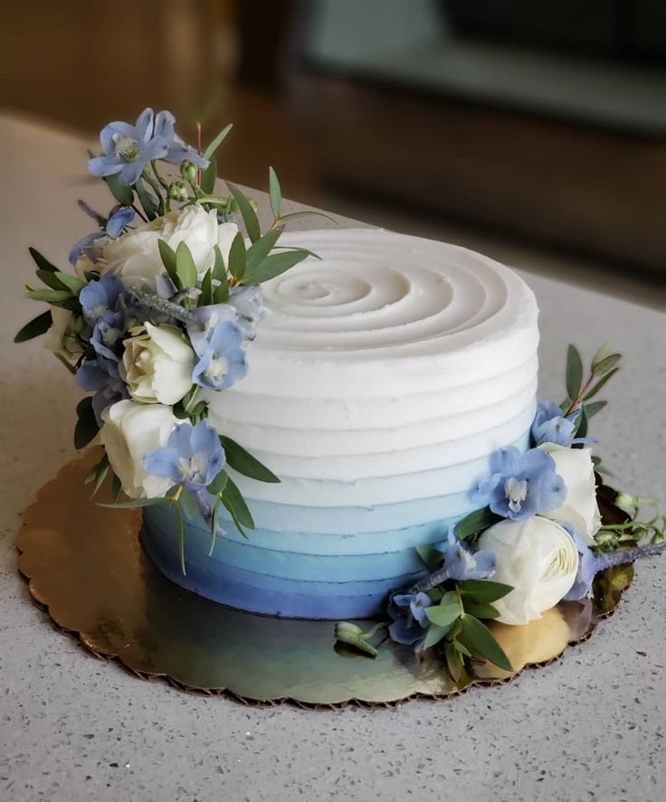 there is a white cake with blue and white flowers on the top, along with greenery