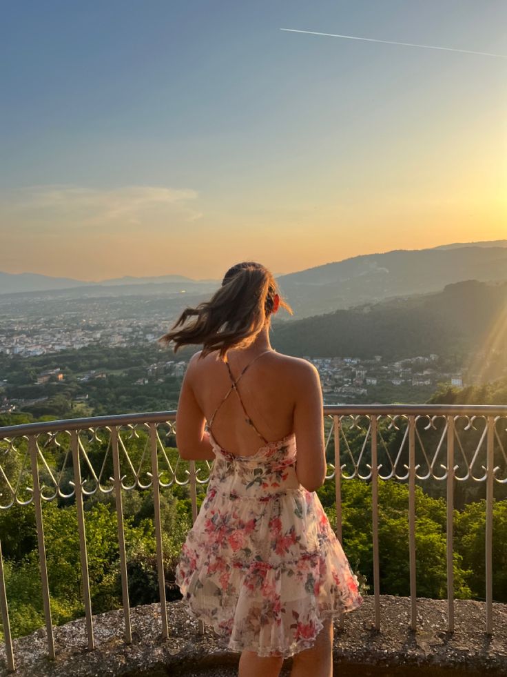 a woman standing on top of a balcony next to a lush green hillside