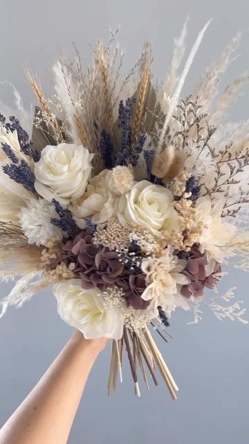 a hand holding a bouquet with white flowers and dried grass in it's center