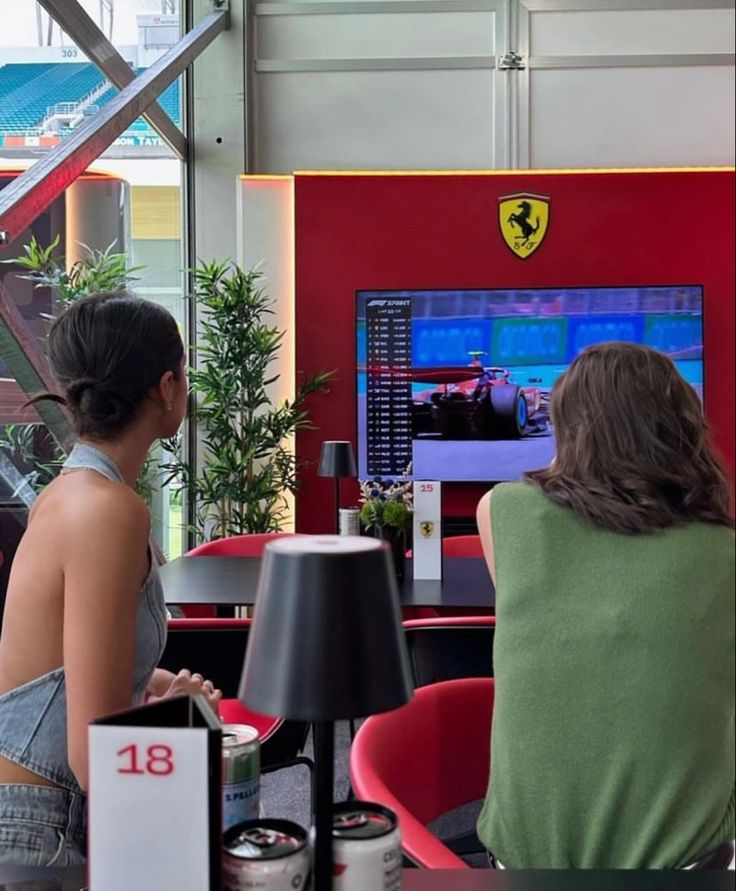 two women sitting in front of a tv playing video games at a restaurant table with ferrari logo on the screen