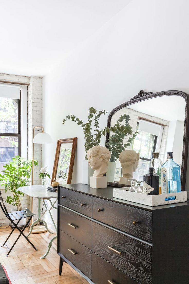 a room with a dresser, mirror and plants