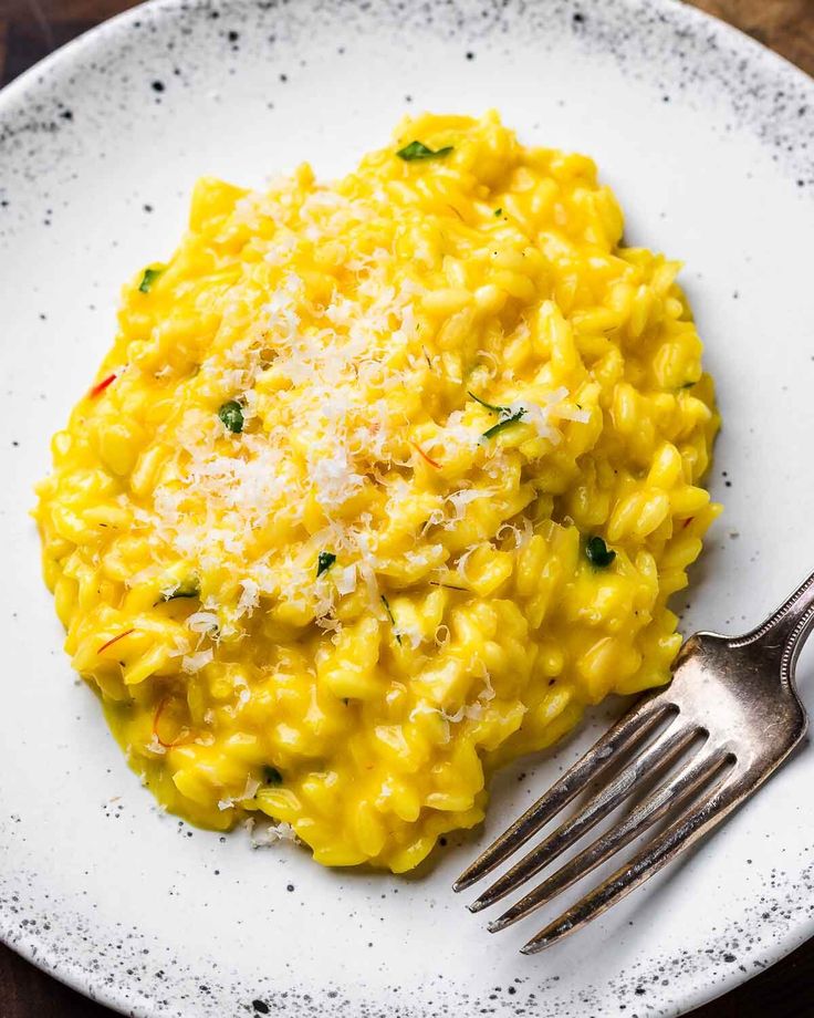 a white plate topped with macaroni and cheese next to a fork on top of a wooden table