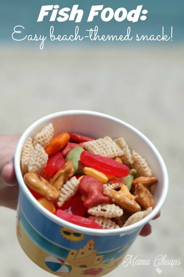 a person holding up a cup filled with cereal and fish food next to the ocean