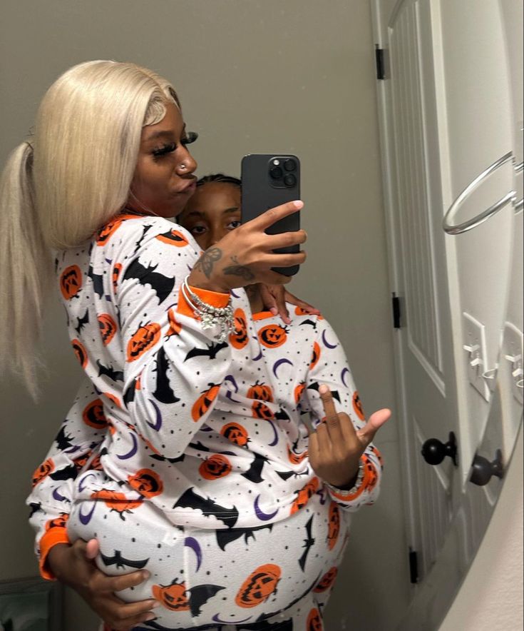 a woman taking a photo of herself in the mirror with her cell phone while wearing a halloween pajama