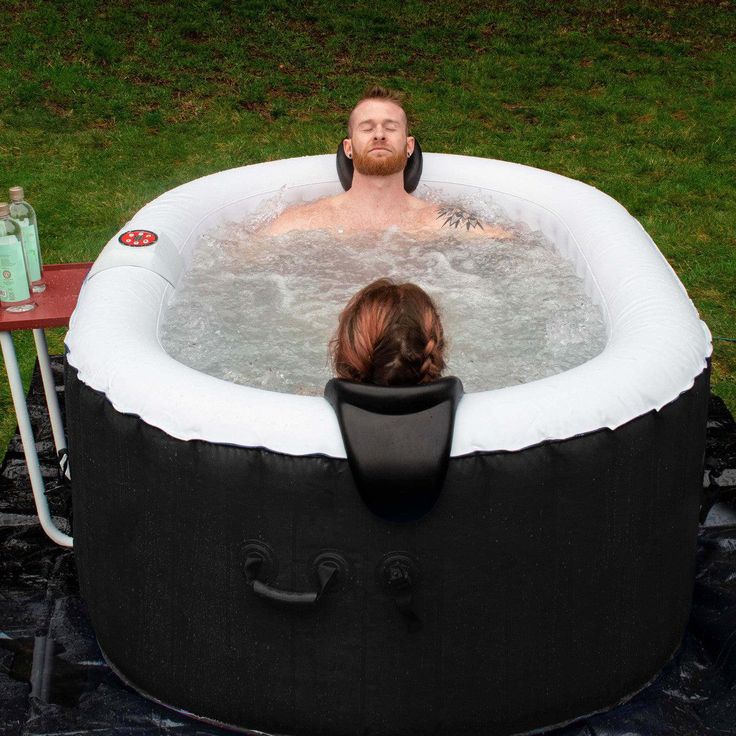 a man sitting in a hot tub on top of a green grass covered field next to a woman