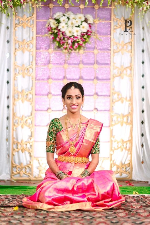 a woman in a pink and green sari sitting on the ground with flowers around her