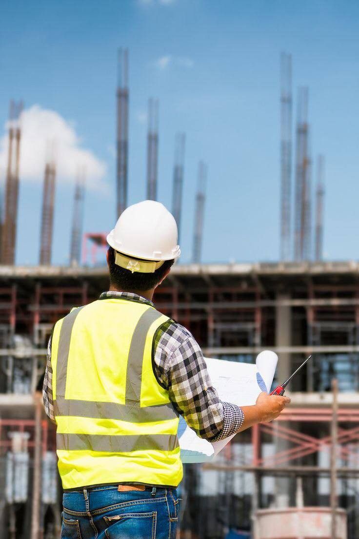 a construction worker holding a piece of paper in front of a large building under construction