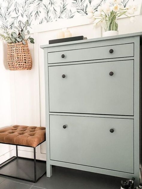 a gray dresser sitting next to a white wall with flowers on it and a brown footstool