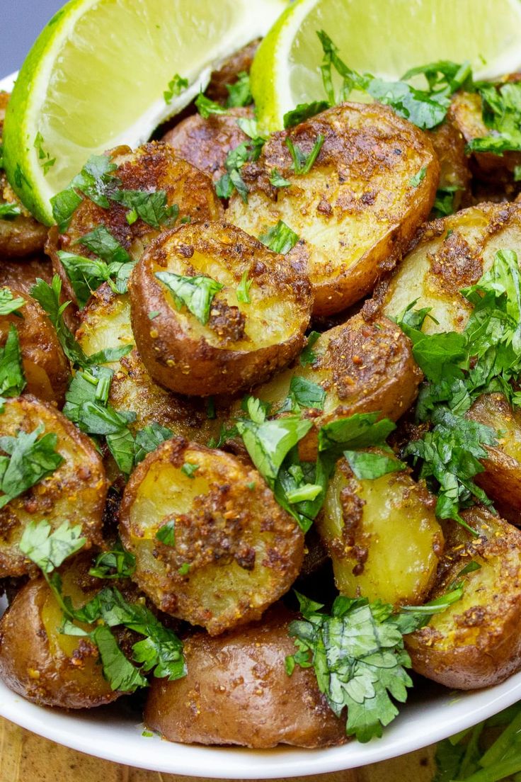 a white bowl filled with potatoes and garnished with cilantro, parsley and lime