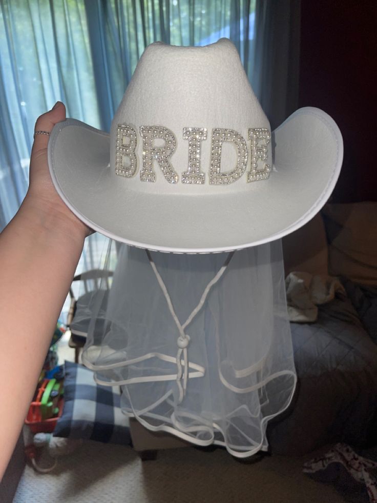 a white hat with the word bride written on it is held by a woman's hand